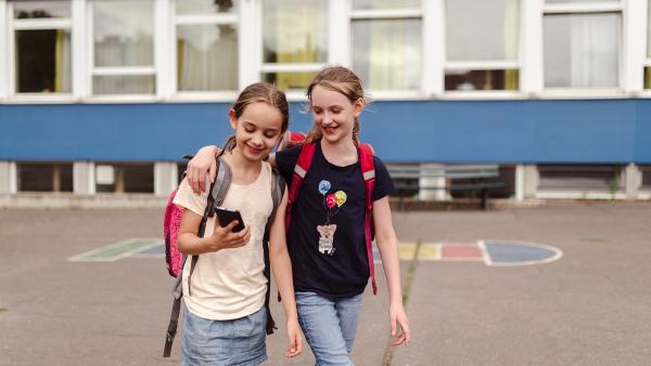 Zwei Mädchen laufen mit einem Smartphone über den Schulhof.