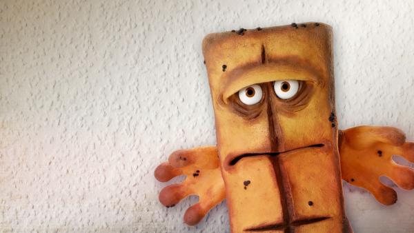 Bernd das Brot steht vor einer tristen Raufasertapete.