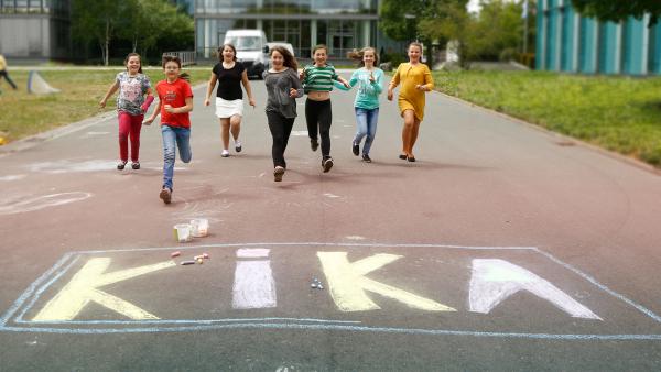 Kinder rennen auf ein KiKA-Logo zu, das mit Kreide gezeichnet wurde.