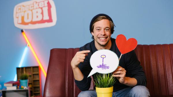 Tobi mit einer Topfpflanze und zwei Emojis