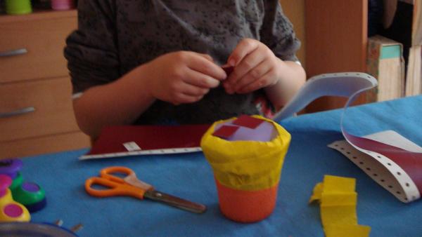 Kind beklebt die Rassel mit buntem Papier