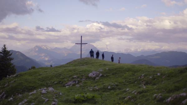 Figuren in der Ferne neben einem Gipfelkreuz in den Bergen