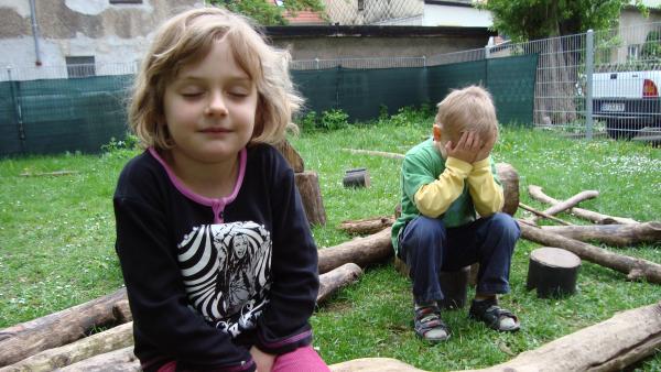 Zwei Kinder sitzen mit geschlossenen Augen im Garten und lauschen den Geräuschen.