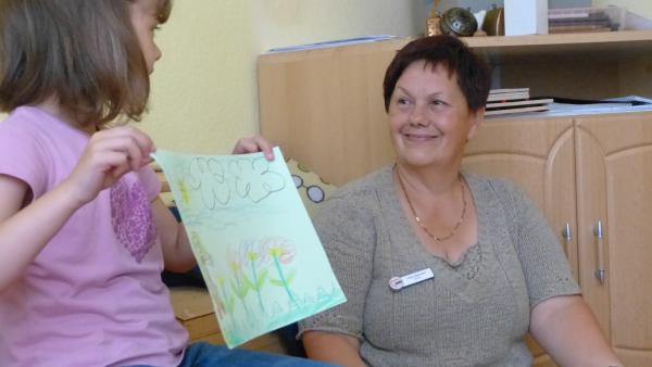 Mädchen präsentiert ihr Bild vor Erzieherin