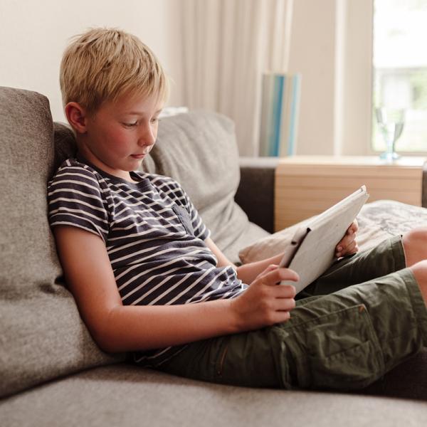 Ein Junge sitzt mi enem Tablet auf einer Couch.