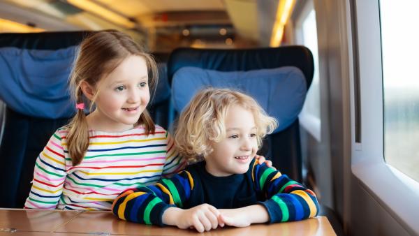 Ein Mädchen und ein Junge im Kindergartenalter sitzen in einem Zug und schauen aus dem Fenster.