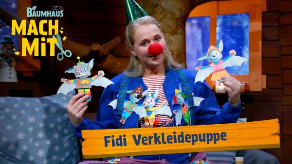 Eine blonde Frau trägt ein weiß-rot-gestreiftes Shirt, eine blaue Jacke, einen grünen Partyhut und eine rote Clownsnase. In den Händen hält sie Anziehpuppen aus Papier. 