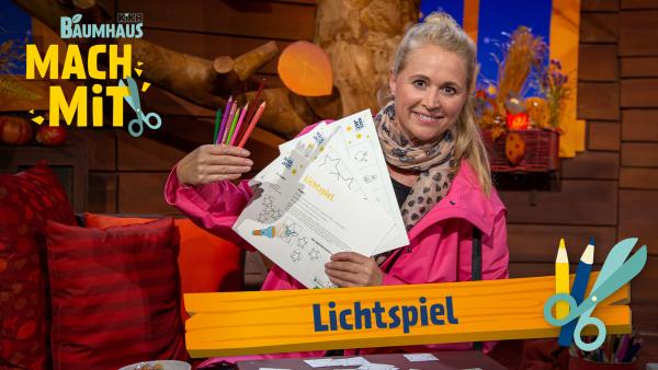 Eine blonde Frau (Singa) hält Buntstifte und den Bastelbogen für das Lichtspiel in der Hand.