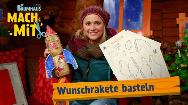 Eine blonde Frau (Singa) mit einer Strickmütze hält eine gebastelte Rakte und Bastelvorlagen in der Hand. 