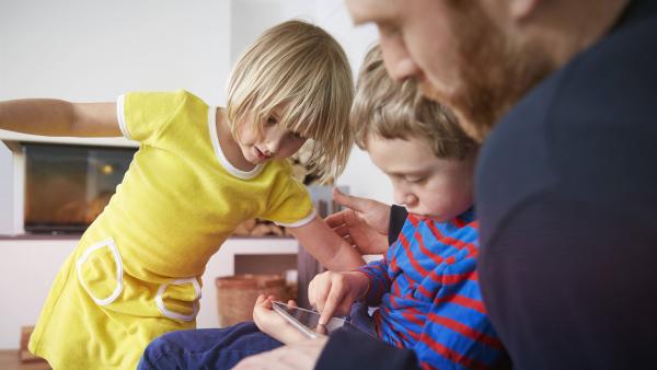 Ein Mann spielt mit seinen zwei Kindern am Tablet.