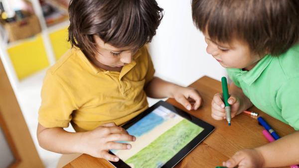Zwei Jungen schauen auf ein Tablet, das auf dem Tisch liegt.