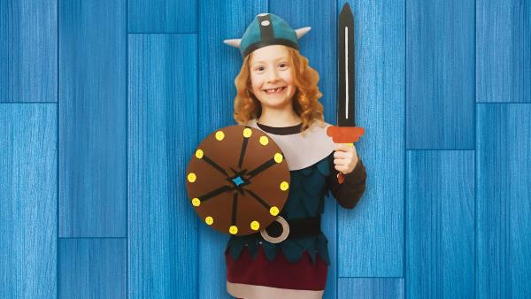 Ein Mädchen in einem Wickie Kostüm mit Schwert und Schild in den Händen