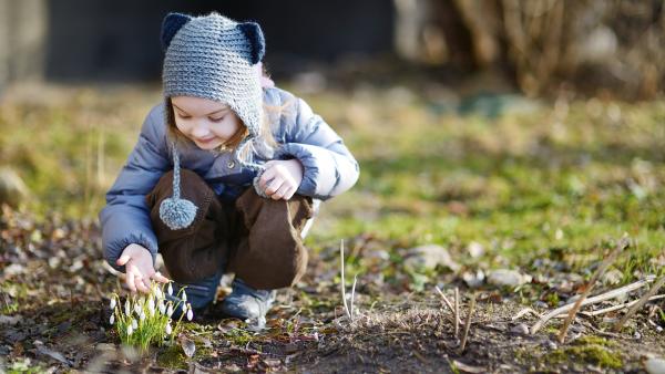 Ein Kind hockt auf einer Wiese und betrachtet weiße Blumen.