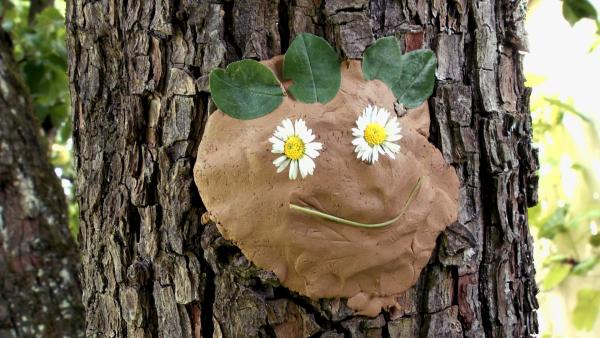 Ein Gesicht aus Ton auf einem Baum, verziert mit Blumen und Blättern 