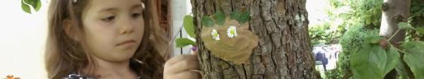 Ein Gesicht aus Ton auf einem Baum, verziert mit Blumen und Blättern 