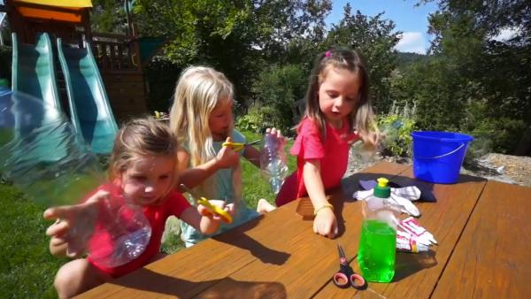 Melina, Karina und Gloria machen Regenbogenschaum mit Plastikflaschen, Lebensmittelfarbe und Seifenlauge. Sie schneiden den Boden der Flaschen ab 
