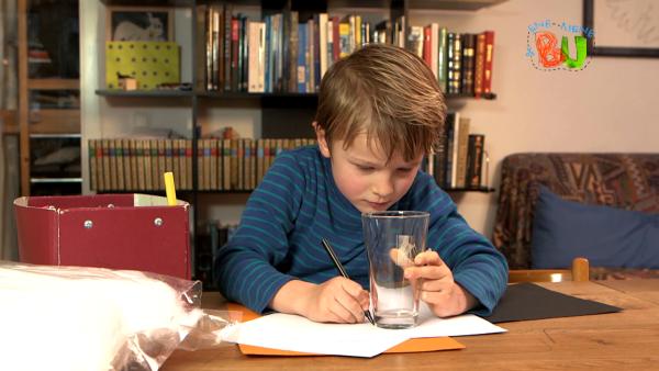 Lasse malt mithilfe eines alten Glas Kreise auf ein weißes Blatt Papier. 