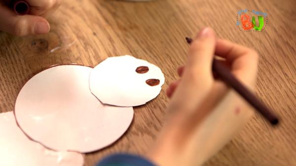 Lasse malt mit einen braunen Stift, dem Schneemann aus Papier Augen auf.