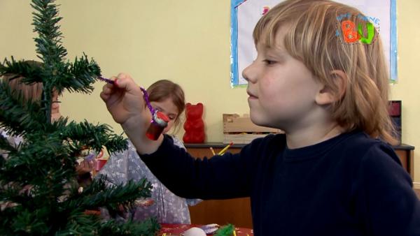 Auf dem Bild seht ihr ein kleines Kind, der den gebastelten Weihnachtsschmuck in den Tannenbaum hängt.