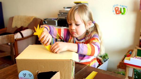 Ein Mädchen befestigt die gelbe Sternschnuppe in den Schlitz des Pappkartons ein. 