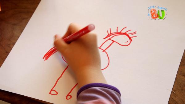 Ein Kind malt auf weißes Papier einen Esel drauf. 