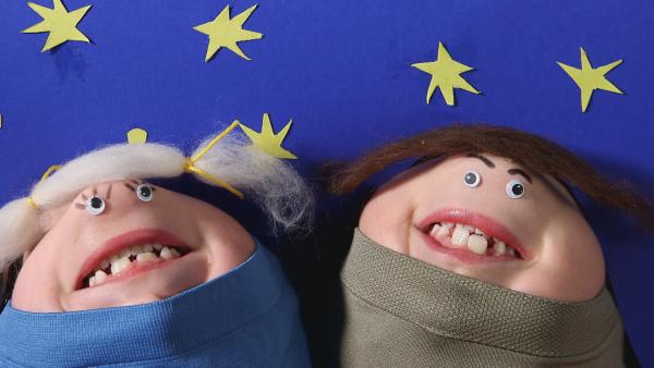 Zwei Kinngesichter in Form von Personen vor einem gebastelten blauen Hintergrund mit gelben Sternen. 