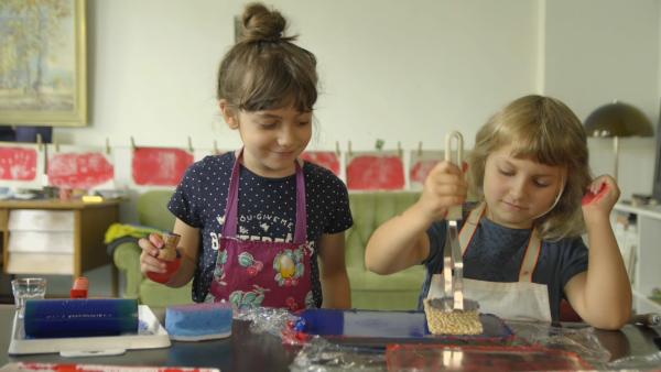 Zwei Kinder legen verschiedene Materialien auf die Gelatineplatte.