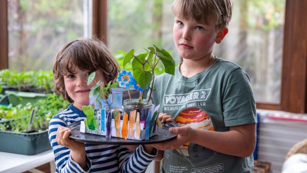 Zwei Jungs zeigen ihren selbstgebastelten Fenstergarten aus Papier rund Einmachgläsern. 