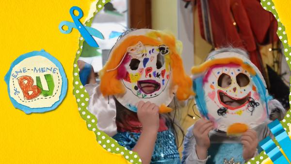 Nina, Mia und Anna haben Papptellermasken gebastelt und zeigen die bunten Masken bei ENE MENE BU. 