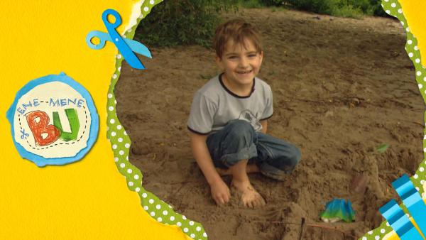 Ein Junge sitzt im Sand und baut eine Sandburg. 