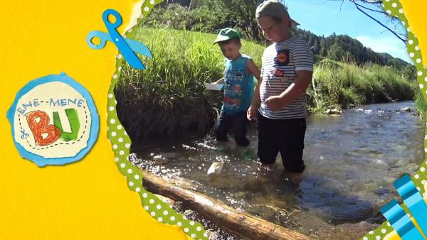 Zwei Jungs bauen an einem Bach einen Staudamm.