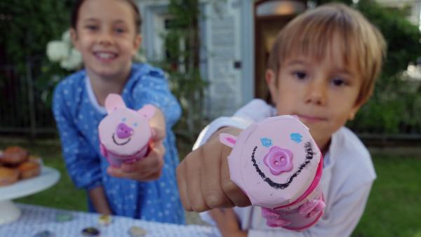 Leni und Sevi, zwei Kinder, halten zwei rosafarbene Klopapierrollen Sparschweine in der Hand.