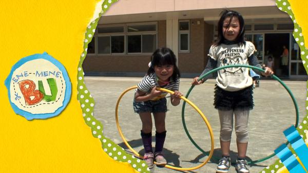 Zwei Mädchen auf einem Schulhof mit Hula Hoop Reifen. 