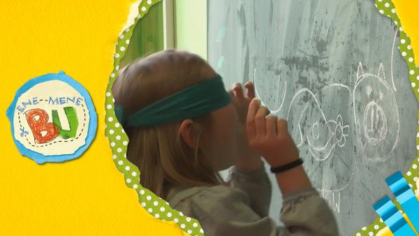 Ein Mädchen mit verbundenen Augen vor einer Schultafel. 