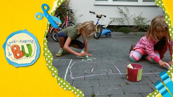 Zwei Kinder malen mit Kreide eine Straßenspiel.