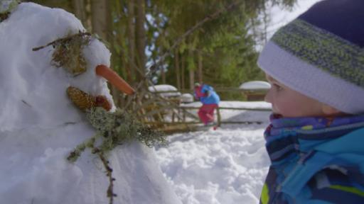 David schaut sich seinen Schneemann an. Der hat eine Möhre als Nase, der Mund ist ein Tannenzapfen und für die Augen hat er Moos genommen.