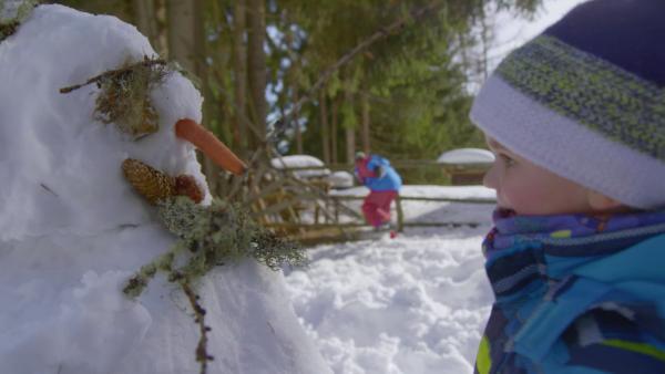 David schaut sich seinen Schneemann an. Der hat eine Möhre als Nase, der Mund ist ein Tannenzapfen und für die Augen hat er Moos genommen.
