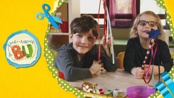 Jane und Suvi zeigen ihre gebastelten Zauberstäbe. Die Stäbe sind mit Kreppapier umwickelt und mit einem Stern beklebt. 