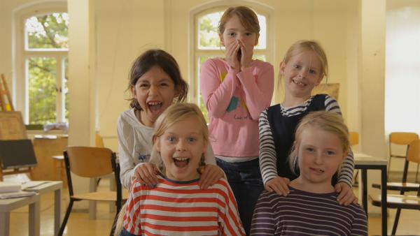 Fünf Mädchen stehen aufgereiht und lachen in die Kamera. Das mittlere Kind hält die Hände vors Gesicht.