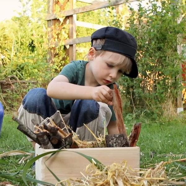 Ein Junge sitzt in einem Garten und sammelt Holz in einer Schale.