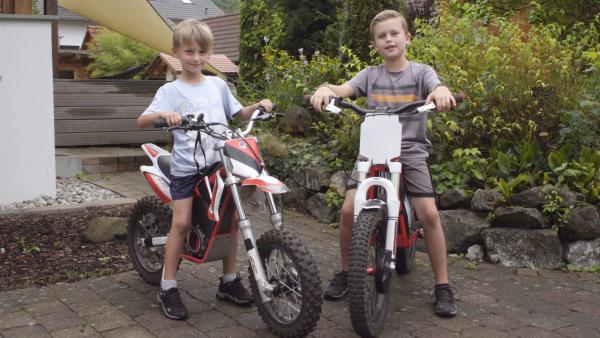 Zwei Vorschulkinder sitzen auf je einer Motorcrossmaschine für Kinder.