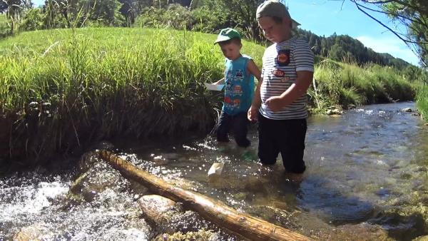 Jonathan und Paul setzen Papierboote ins Wasser.