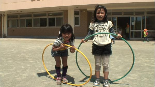 Zwei Mädchen stehen auf einem Hof und haben je einen Hula Hoop Reifen in der Hand.