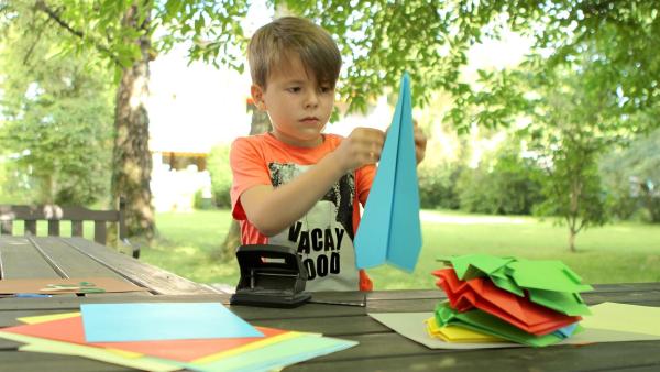 Adnan faltet einen blauen Papierflieger.