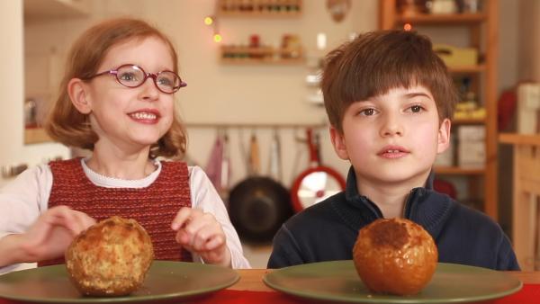 Ein Junge und ein Mädchen sitzen am Tisch. Vor ihnen stehen zwei Bratäpfel auf Tellern.