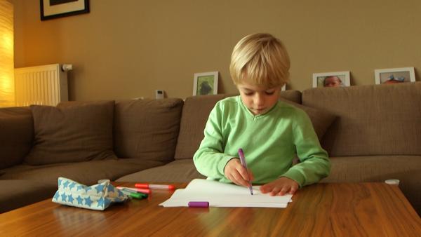 Ein Junge sitzt an einem Wohnzimmertisch und malt ein Bild.
