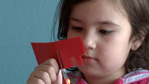 Ein Mädchen schneidet verschiedene Formen aus rotem Papier aus.