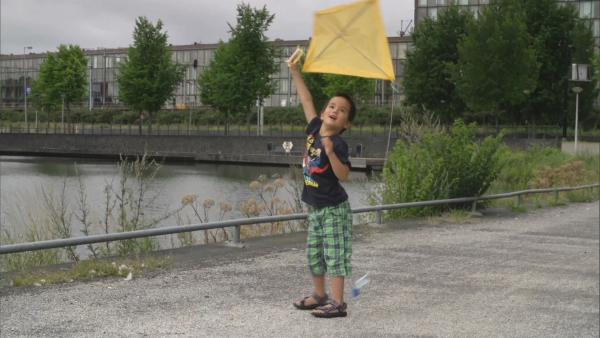 Ein Junge hält einen gelben Drachen über seinen Kopf.