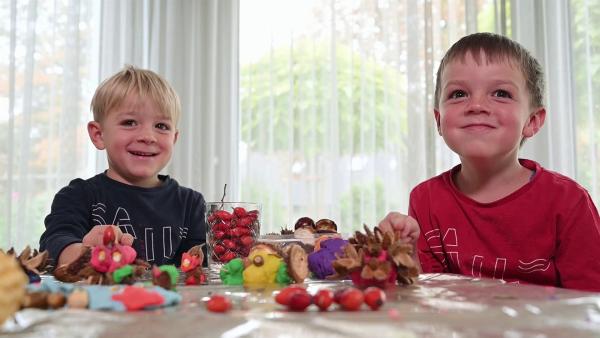 Zwei Jungs sitzen am Tisch und schauen sehr glücklich. Vor ihnen liegt herbstliche Deko.