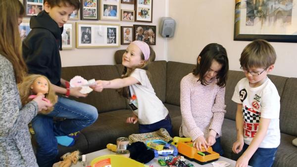 Fünf Kinder stehen im Wohnzimmer. Vor ihnen auf dem Tisch liegen verschiedene Sachen und eine Kasse.